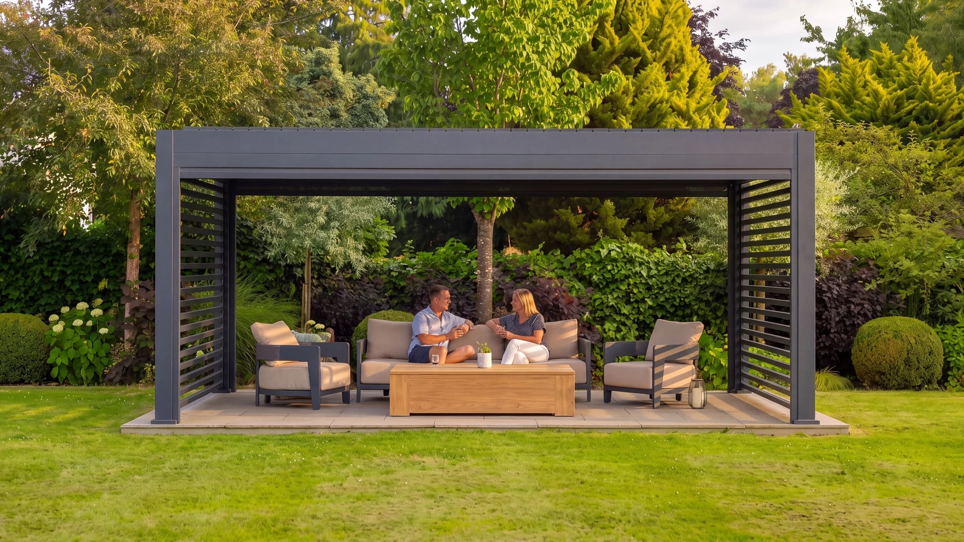 A couple relaxing beneath a furnished LuxSol pergola in a landscaped garden