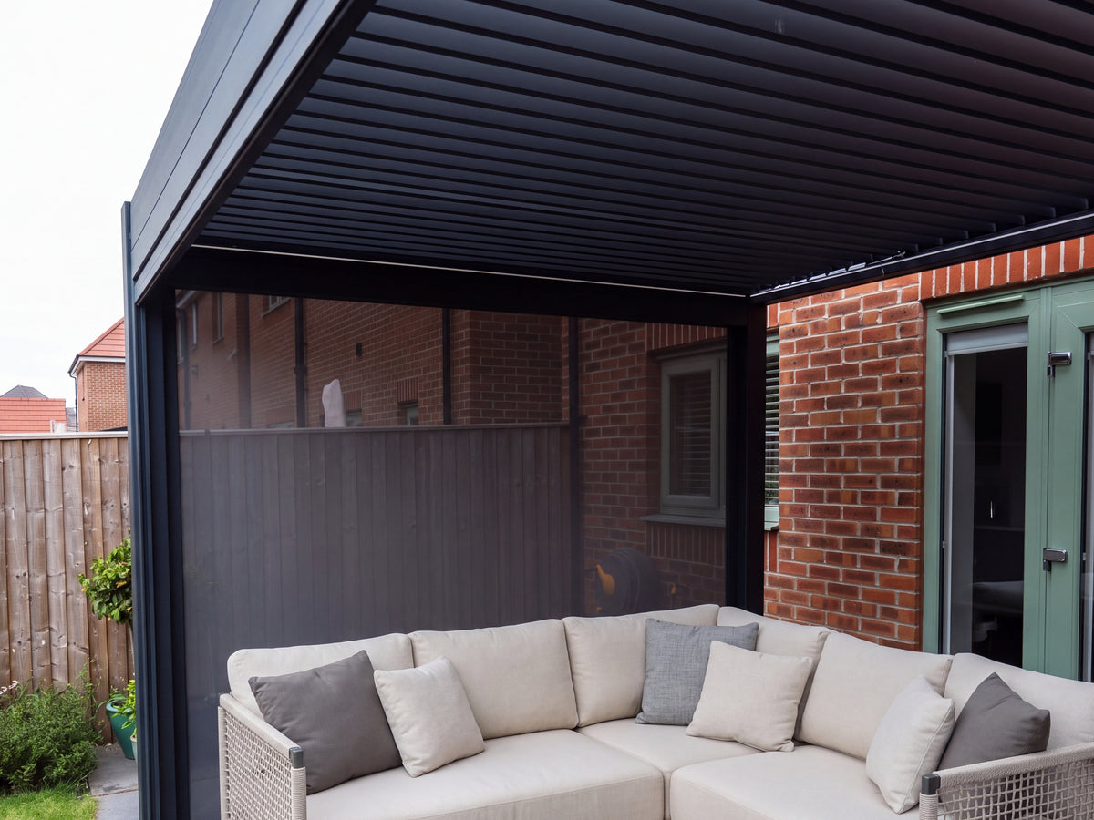 View beneath the Como roof showing aligned louvres, anthracite frame and a lowered side screen beside a cream sofa.