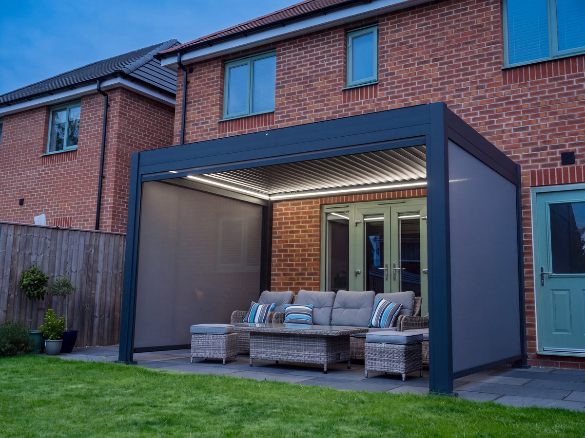 Como pergola beside a brick house with lowered side screens, open louvres and white lighting.