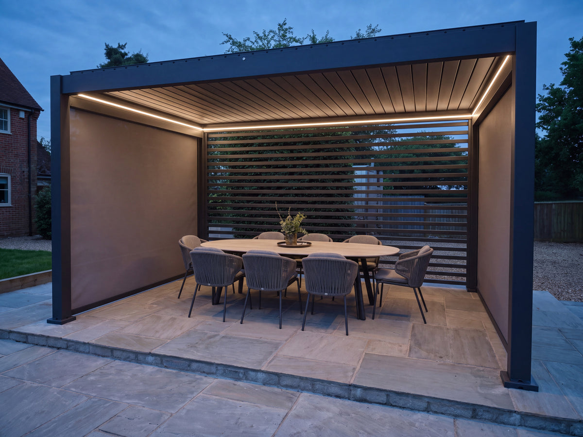 Como pergola at dusk with a closed roof, lowered side screens and white lighting above an outdoor dining table.