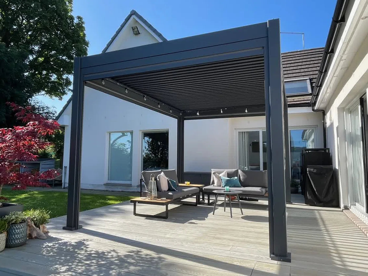 Aura pergola with seating on a patio beside a white house