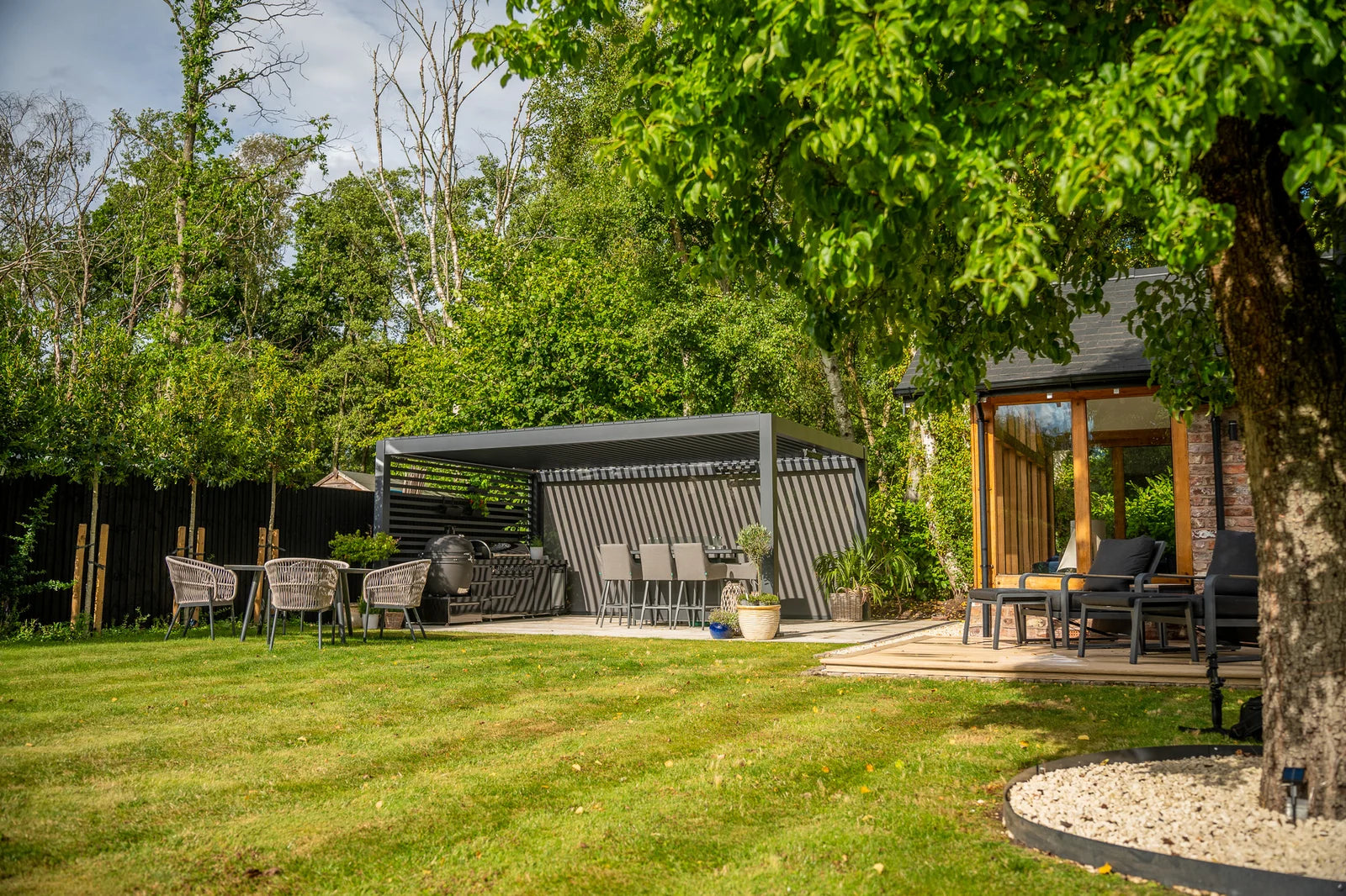 A LuxSol Tora pergola with an outdoor kitchen and dining space in an established garden