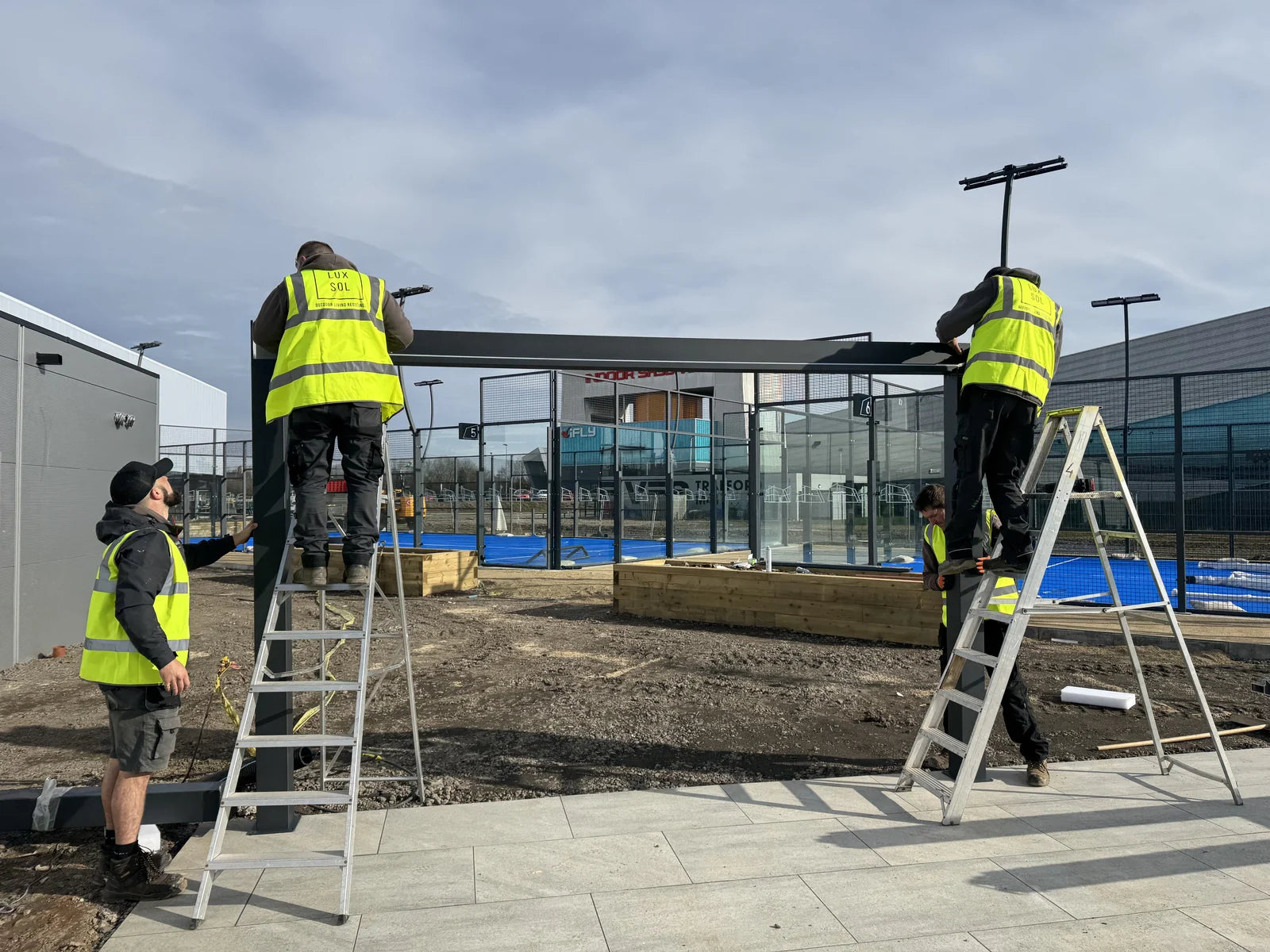 Four LuxSol installers assembling the aluminium pergola frame at The Padel Club, TraffordCity