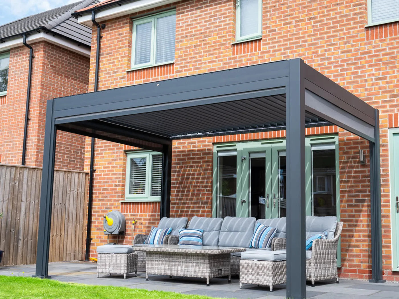 Como pergola and corner sofa on a patio beside a brick house